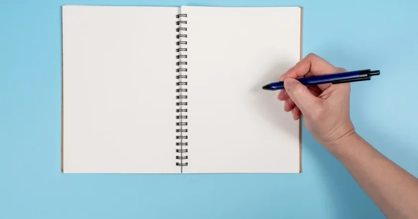 Cahier à spirales vierge, vide, avec main droite qui tient un stylo bleu @ apinya / stock.adobe.com