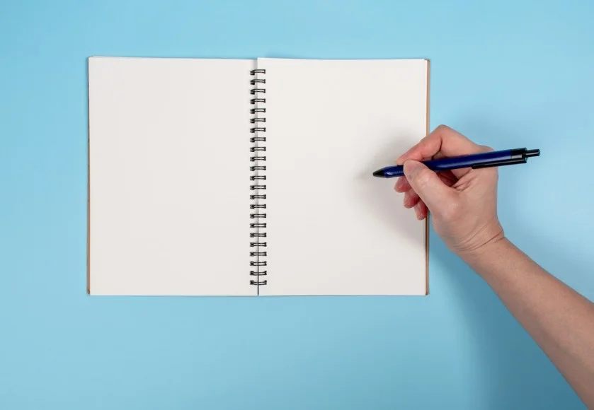 Cahier à spirales vierge, vide, avec main droite qui tient un stylo bleu @ apinya / stock.adobe.com